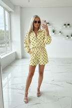 Woman in a yellow polka dot outfit taking a selfie in a bright room.